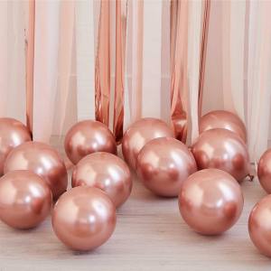 Image of multiple rose gold latex balloons on the floor with rose gold tassels behind them.