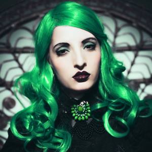 Image of a woman wearing a shoulder length green costume wig with curls and a side part.