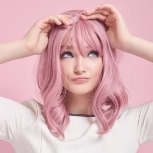 Image of a woman wearing a blush pink costume wig with a fringe and slight waves.