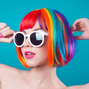 Image of a woman wearing a short bob cut rainbow streaked costume wig.