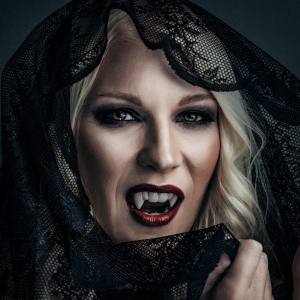 Image of a women wearing a black lace headwrap with red lips and vampire fangs.
