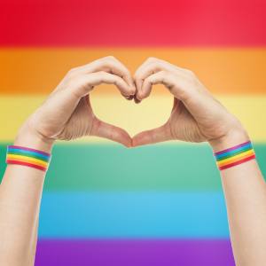 Image of a person making a heart shape with their hands against a rainbow background